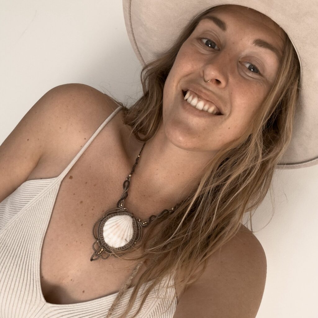 Macrame artist Amber, founder of Namas · Sea, handmade jewelry crafted from shells, crystals and soul. Wearing a boho hat, a white top and a statement shell necklace