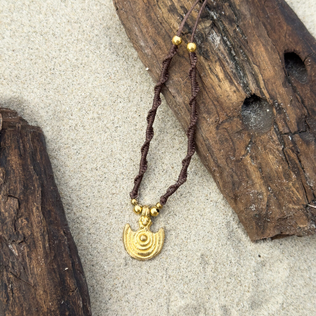 Handmade macrame necklace with brass beads and brass pendants laying on a piece of driftwood on the beach