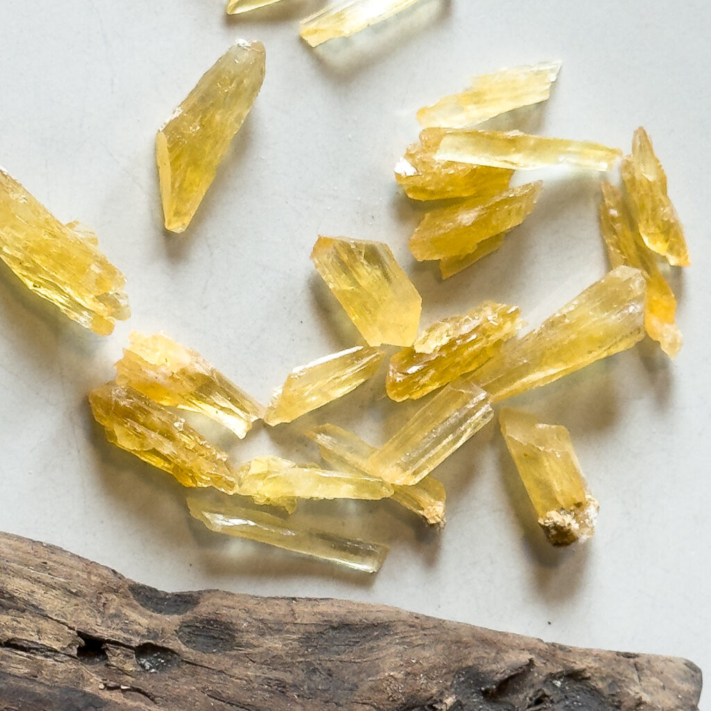 Golden yellow Honey calcite crystal pieces displayed next to a piece of driftwood used for handmade macrame jewelry