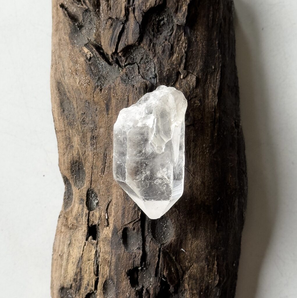 Clear quartz rock crystal on a piece of driftwood, used for handmade jewelry
